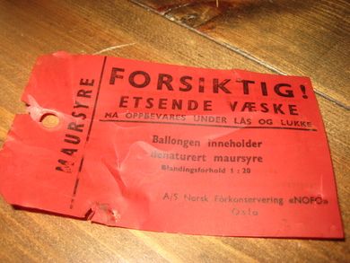 Merkelapp i plast: FORSIKTIG. ETSENDE VÆSKE. MAURSYRE. Fra Norsk Forkonservering 